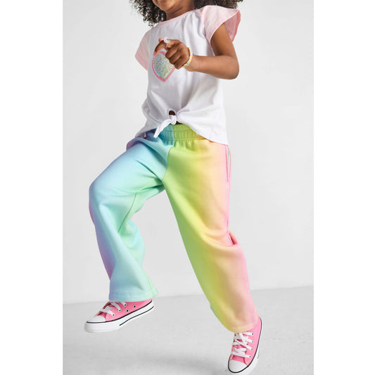 girl skipping, wearing our sustainable rainbow wide-leg joggers and heart knotted baseball tee