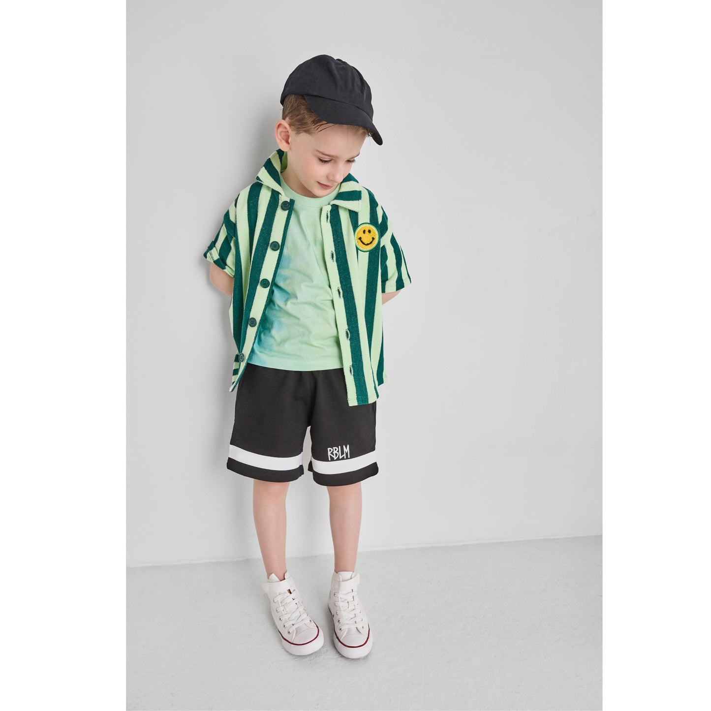 Boy wearing an organic cotton and recycled polyester green striped shirt and black shorts.