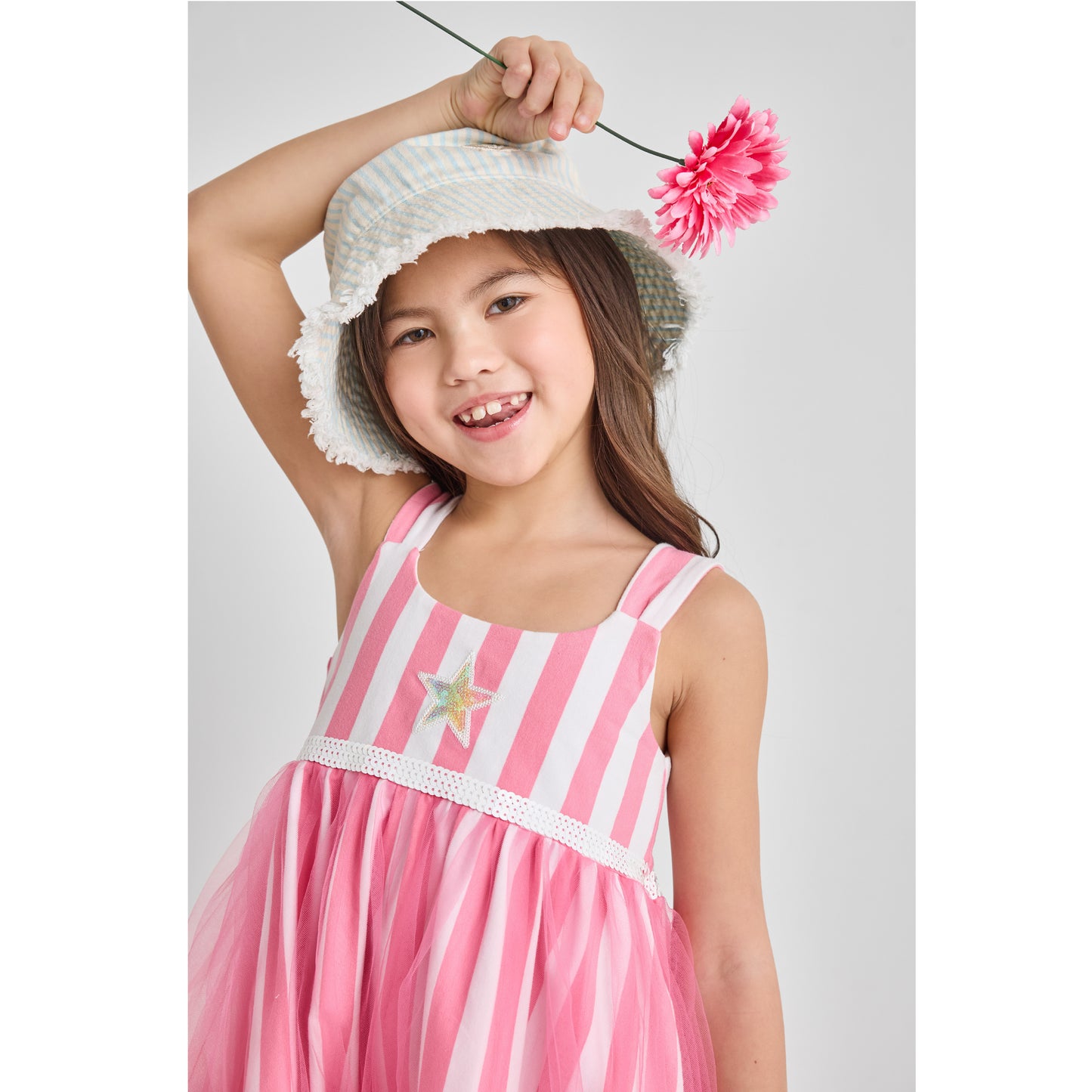 A girl wearing a sustainable striped pink dress with a rainbow star covered in recycled sequins.