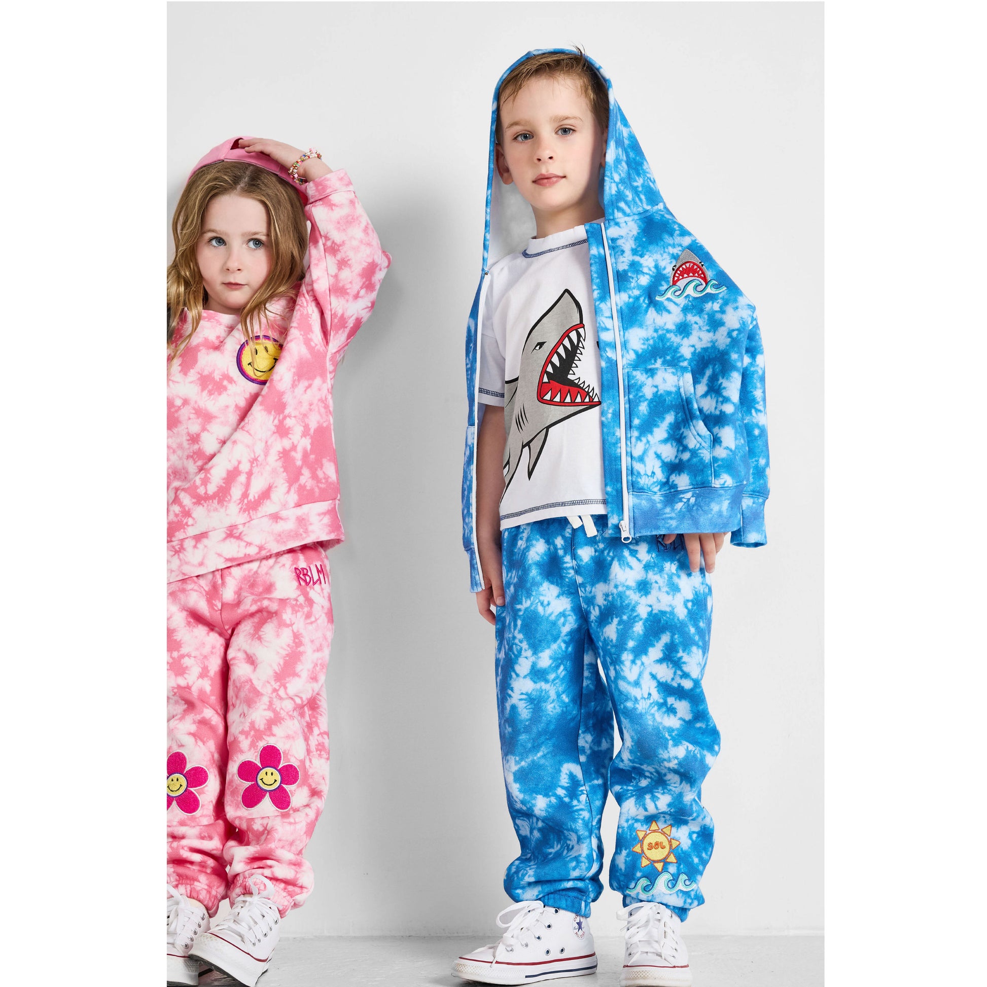 a boy wearing our sustainable shark tee with blue tie-dye ocean joggers and shark blue tie-dye hoodie, and a girl wearing our smiley pink tie-dye set