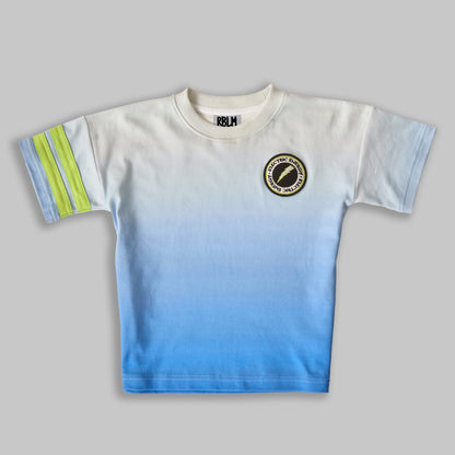 A sustainable, comfortable, and fun t-shirt for children, featuring a white-to-blue ombré pattern with a black and green lightning patch on the left chest and two green stripes on the right sleeve.