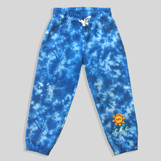 Sustainable, comfortable, and colorful blue and white tie-dye sweatpants for kids, featuring small embroidered waves and a sun with the word 'SOL' inside of it on the lower left leg.
