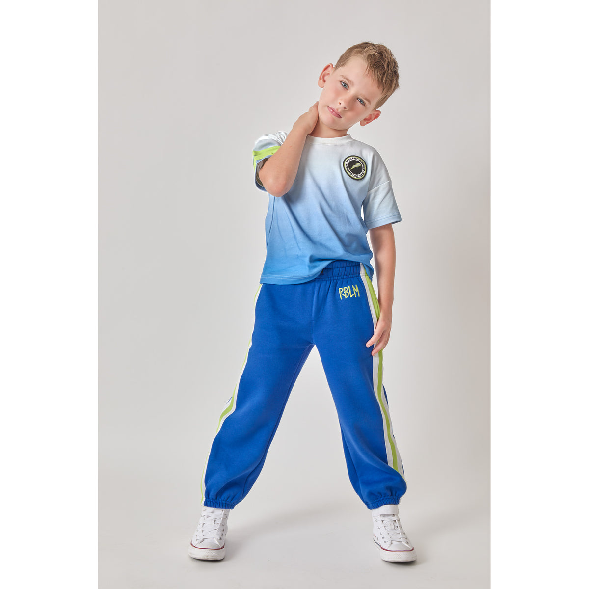 A boy wearing a sustainable organic cotton blue ombré lightning t-shirt, and matching blue sweatpants with green and white side stripes.