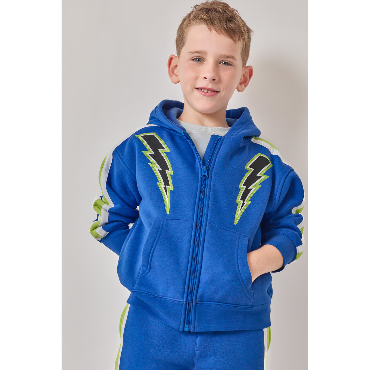 A boy wearing a high-quality, eco-friendly blue zip-up hoodie with black and green lightning bolt graphics on the chest, paired with matching blue sweatpants.