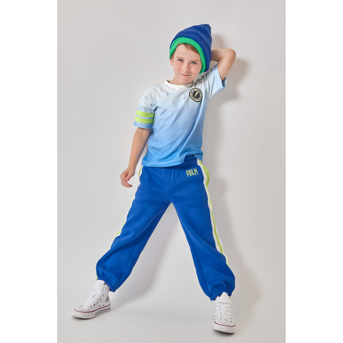 A boy wearing an eco-friendly organic cotton blue ombré lightning t-shirt with green sleeve stripes, and matching blue sweatpants with green and white side stripes.