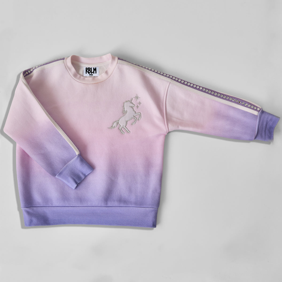 An eco-friendly and comfortable children's long-sleeve crewneck sweatshirt with a pink-to-purple gradient pattern, featuring a white and silver embroidered unicorn on the chest and a recycled rhinestone-embellished stripe down the sleeve, laid flat on a light gray background.