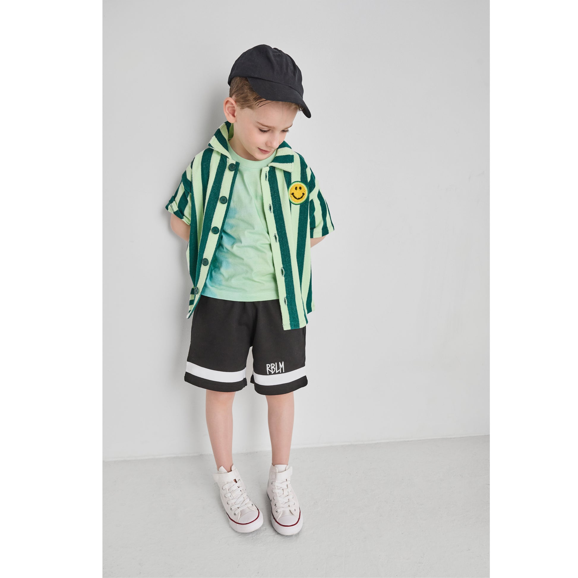 Boy wearing an organic cotton and recycled polyester green striped shirt and black shorts.