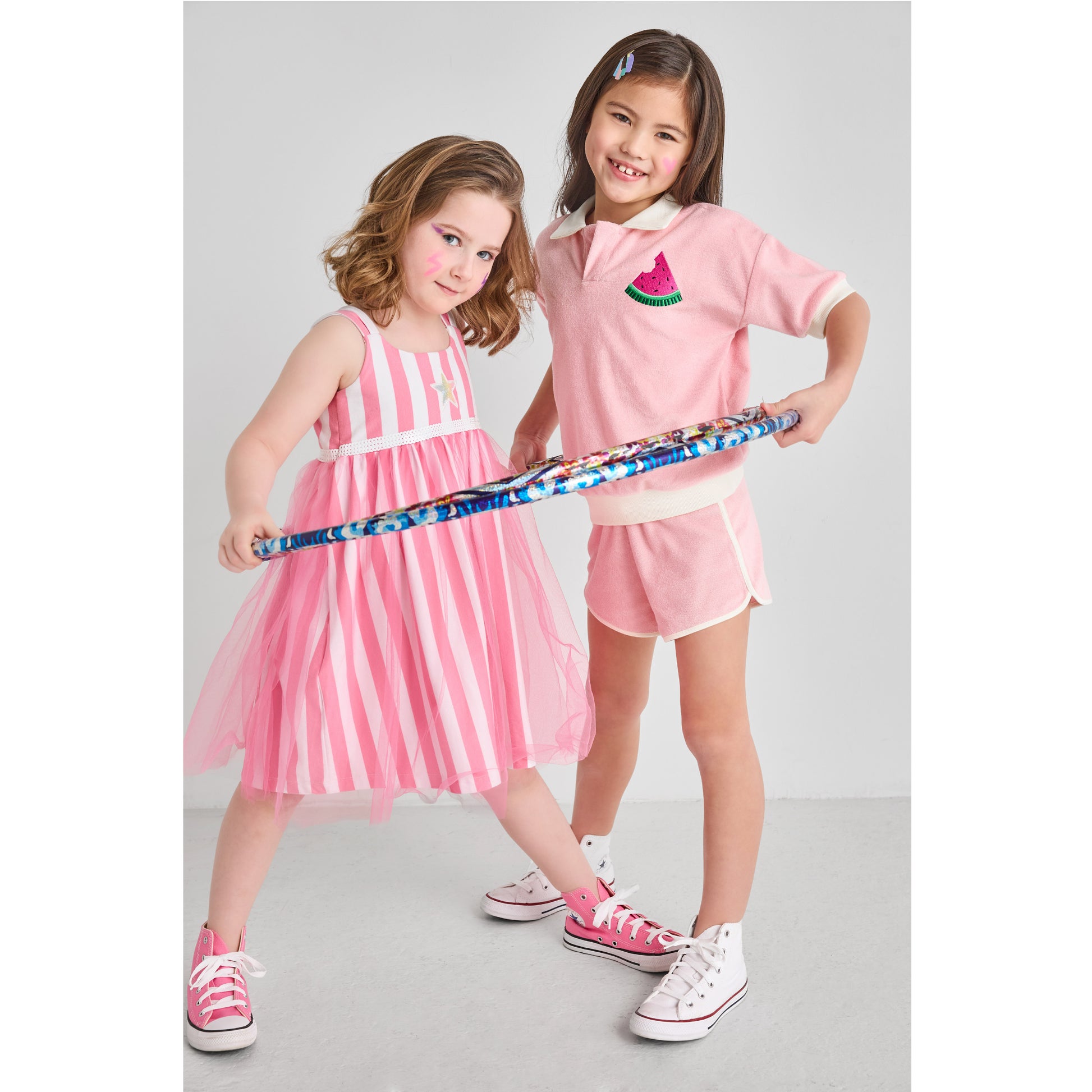Two girls in eco-friendly pink outfits playing with a hula hoop.