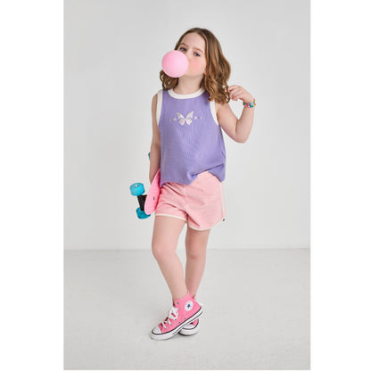 A skateboarding girl wearing a sustainable, purple butterfly tank top and retro pink shorts.