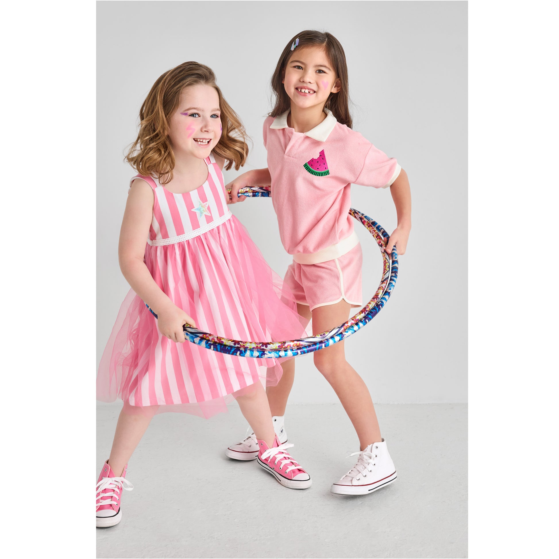 Two girls in cute, bright, sustainable pink outfits with a hula hoop.
