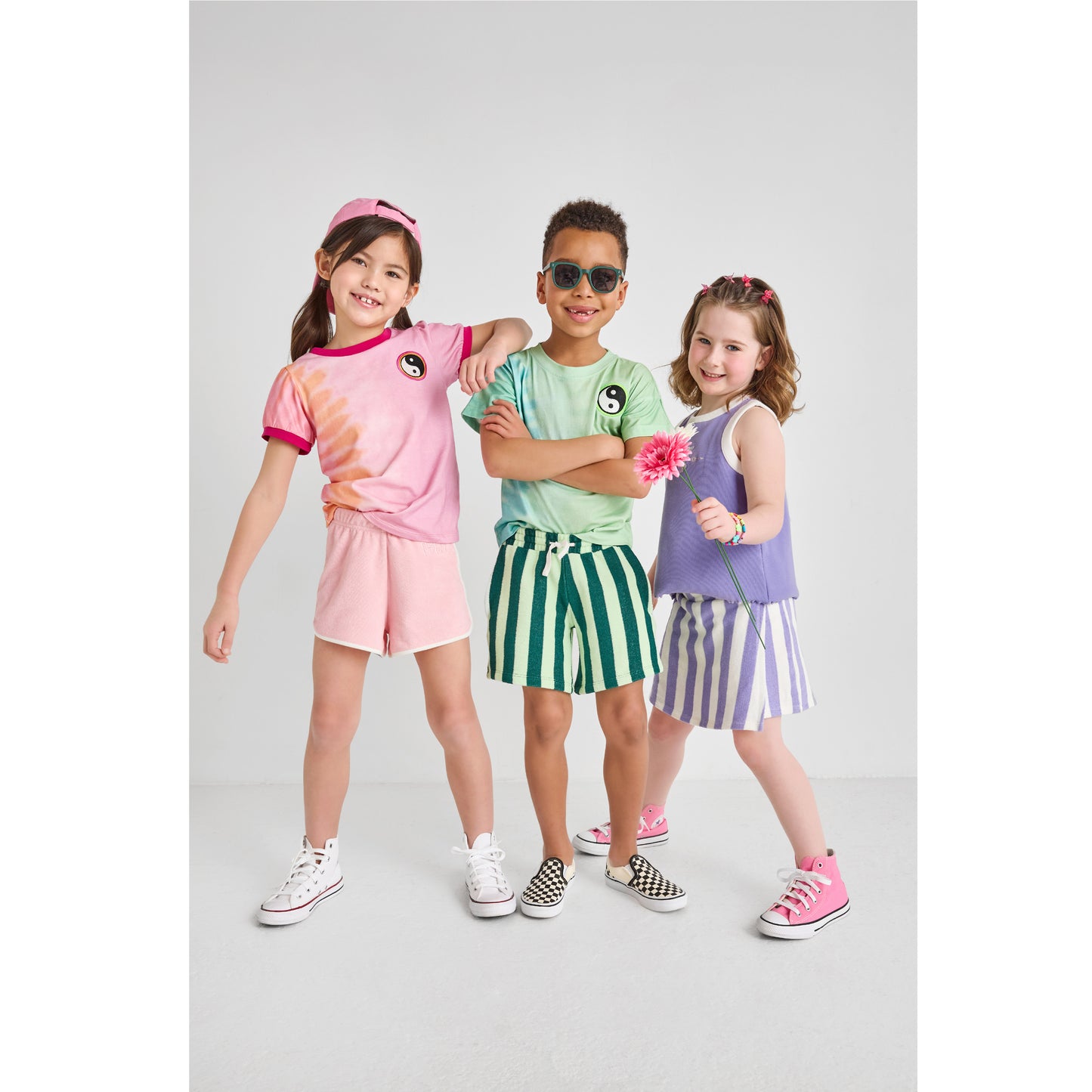 A boy and two girls wearing sustainable, hip, and colorful outfits for summer play.
