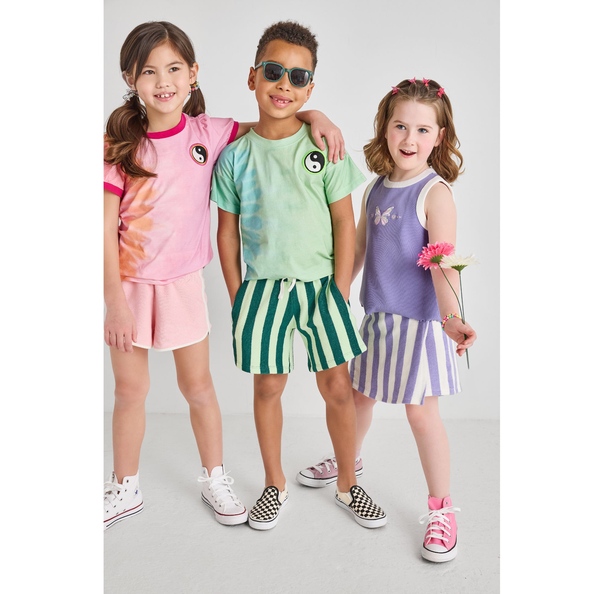 A boy and two girls wearing sustainable, hip, and colorful outfits.