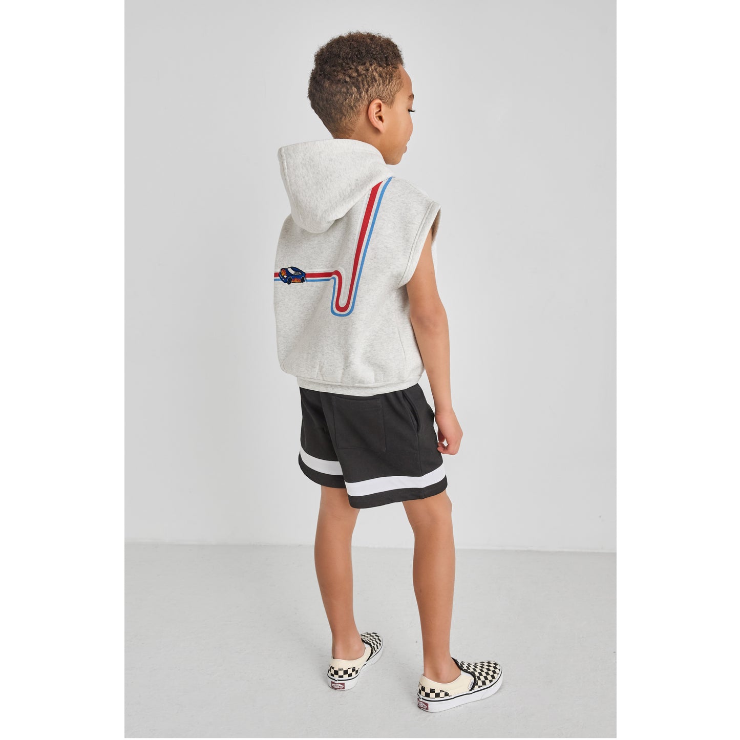 Child wearing a fun, sustainable, race car sleeveless hoodie and black shorts.