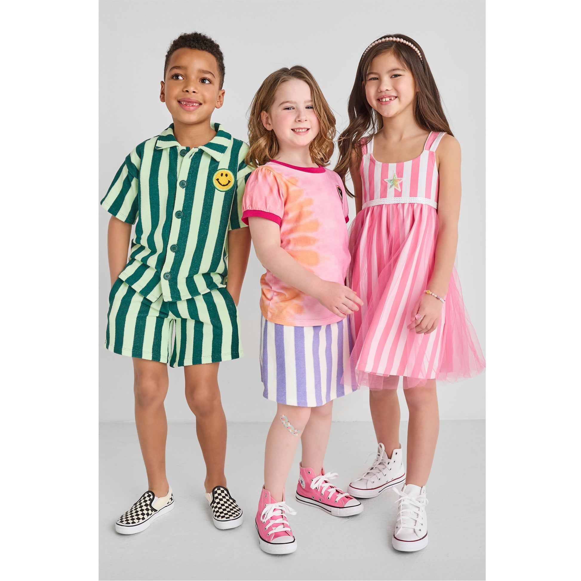 Three children wearing sustainable, colorful striped and tie-dye outfits 