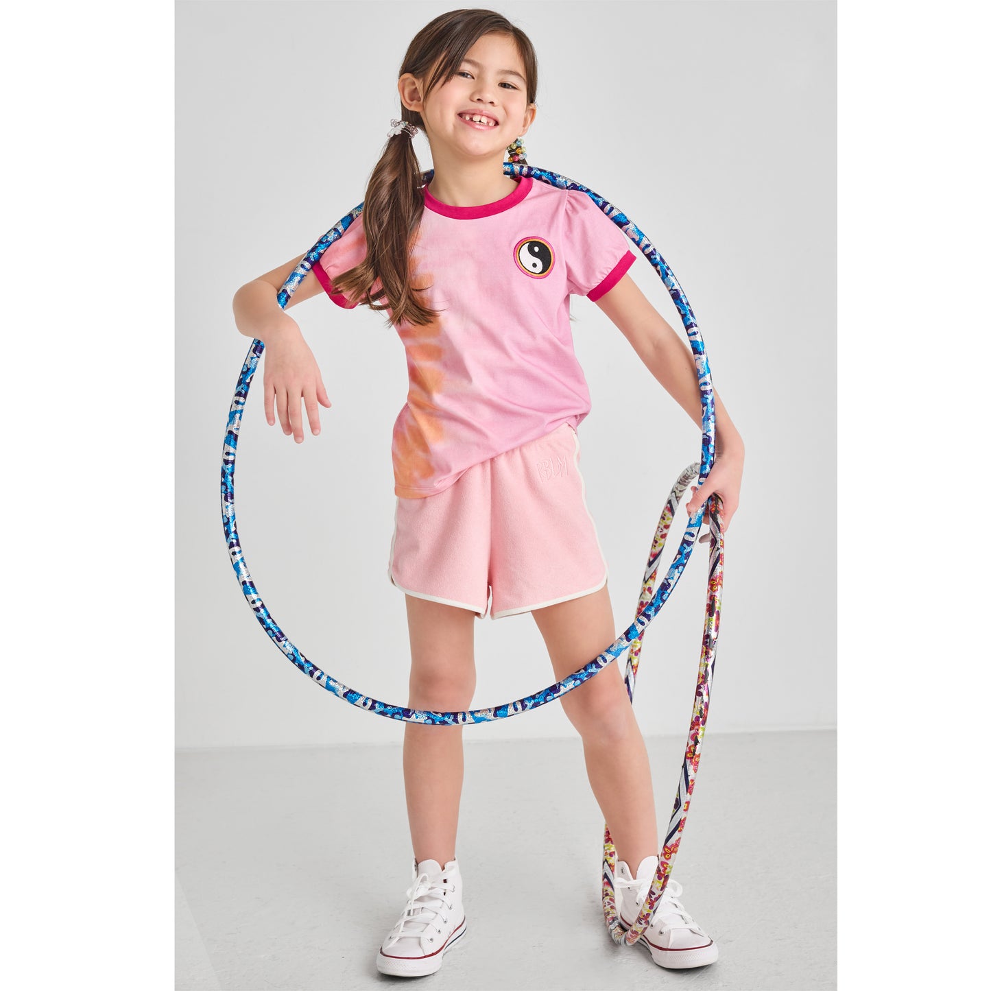 Girl in sustainable, pink summer outfit holding a hula hoop