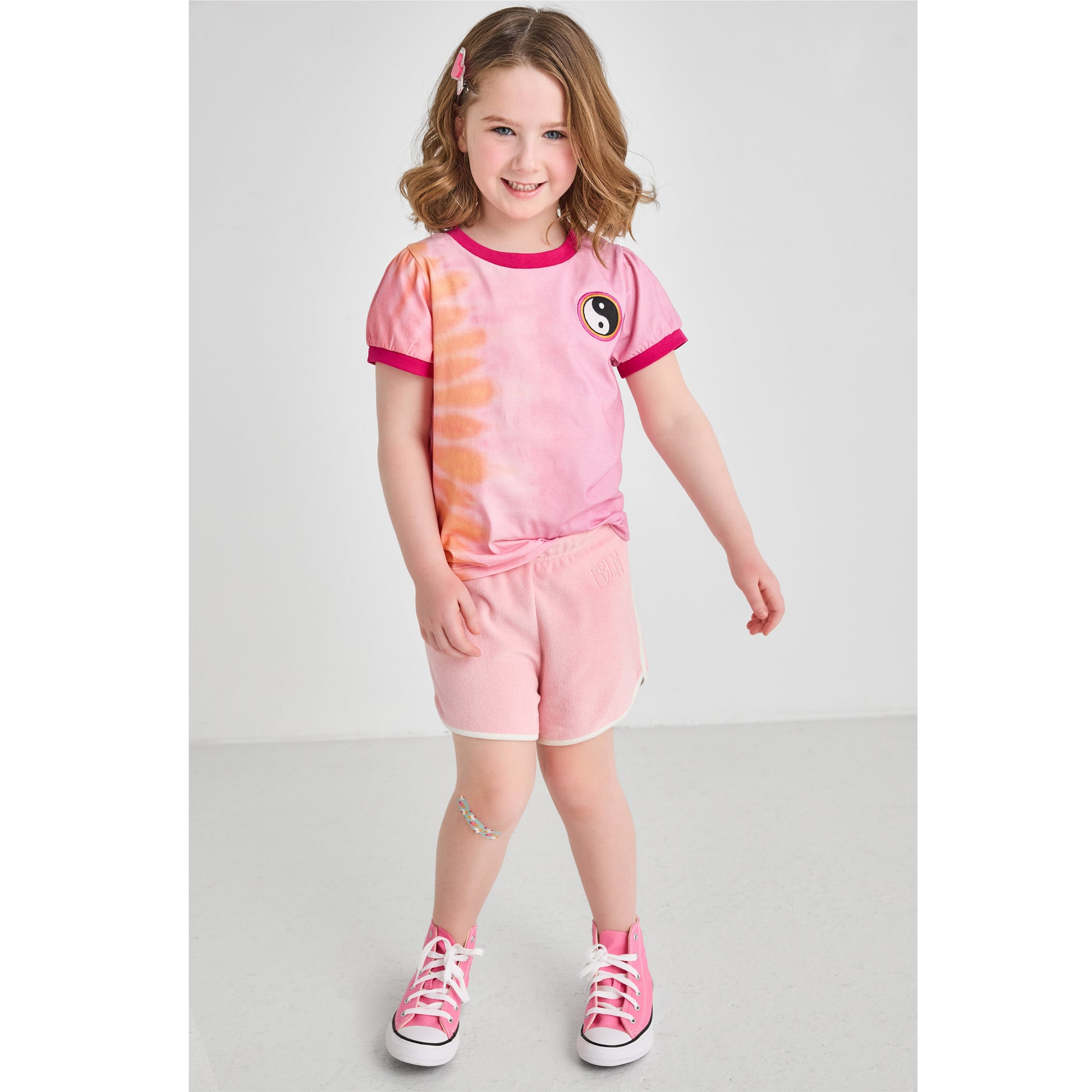 A girl wearing a sustainable pink and orange retro tie-dye t-shirt with pink Terry shorts 