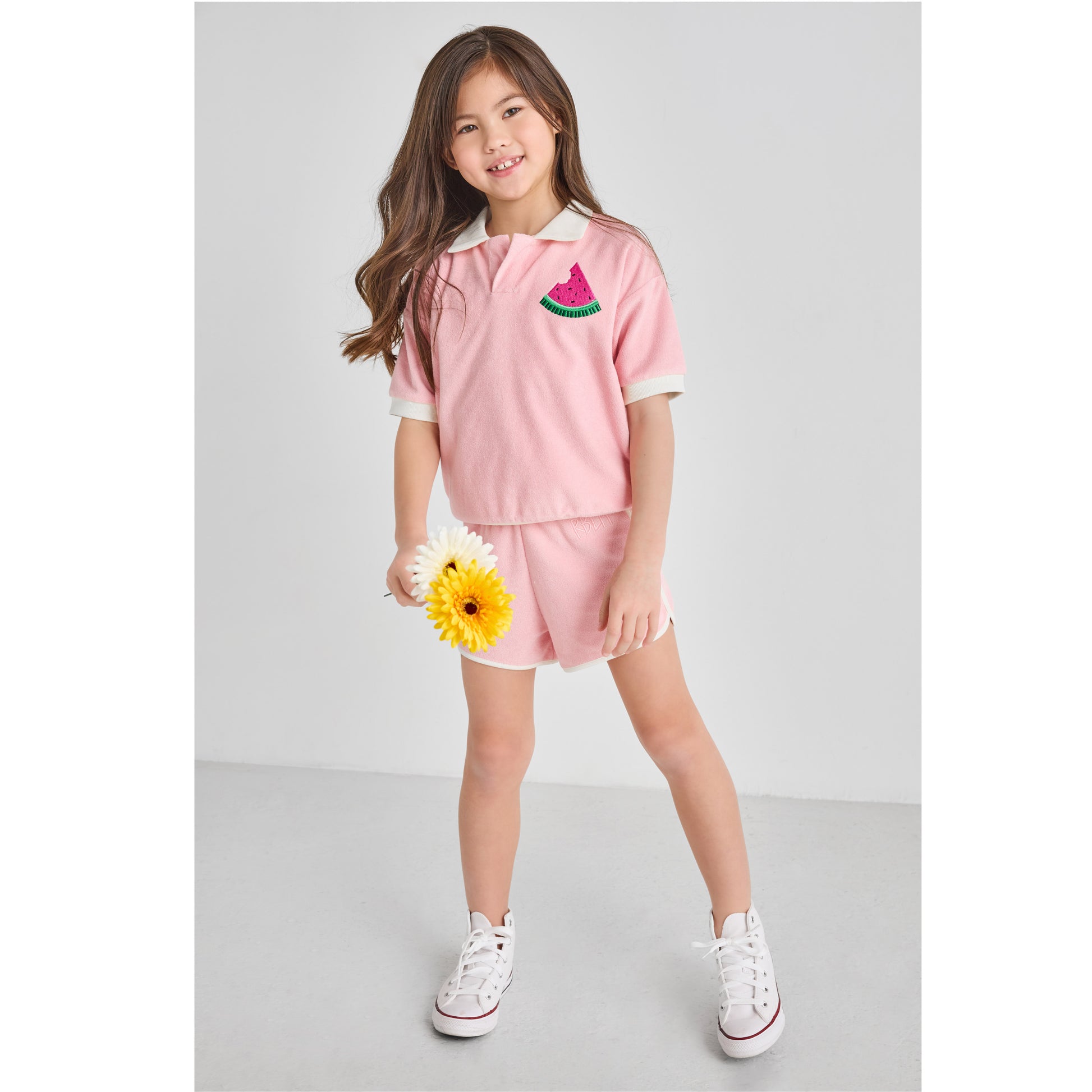 Girl wearing a sustainable, retro, pink Terry outfit with watermelon embroidery, holding daisies.