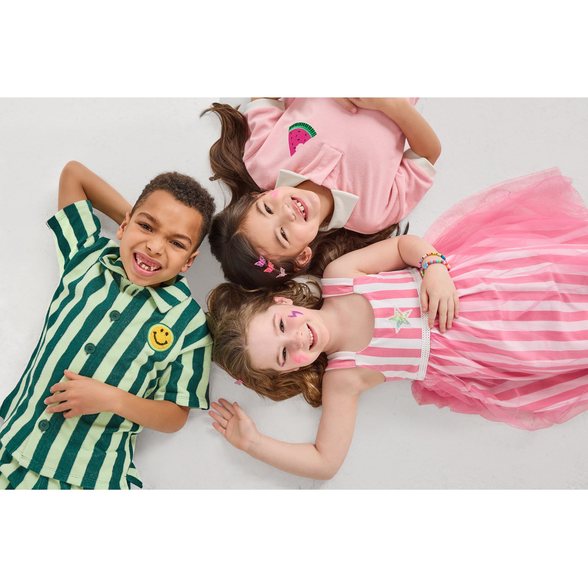 Three children lying on a white surface wearing colorful and eco-friendly outfits.
