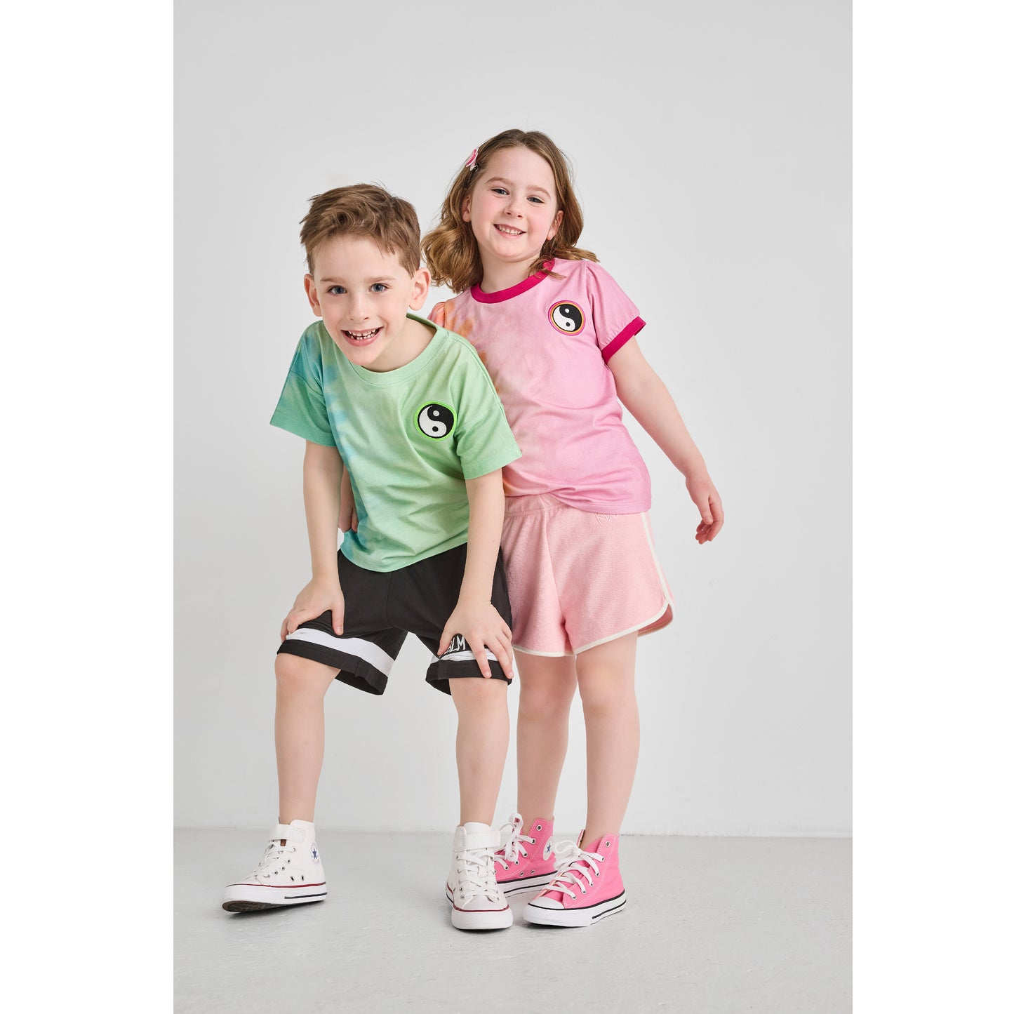 A boy and girl wearing sustainable pink and green tie-dye t-shirts.