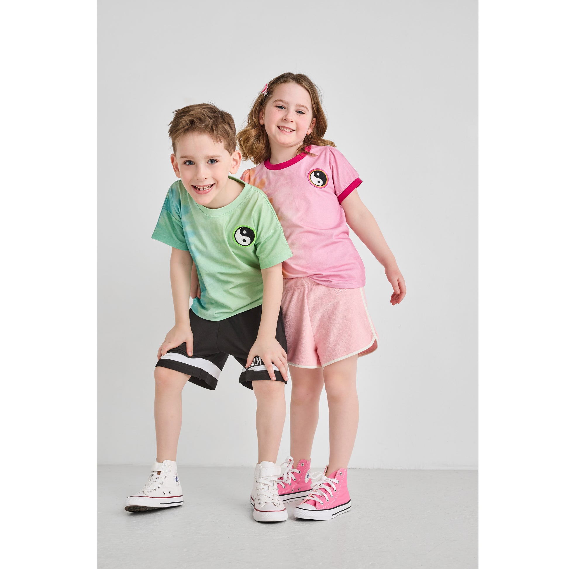 A boy and girl wearing sustainable pink and green tie-dye t-shirts.