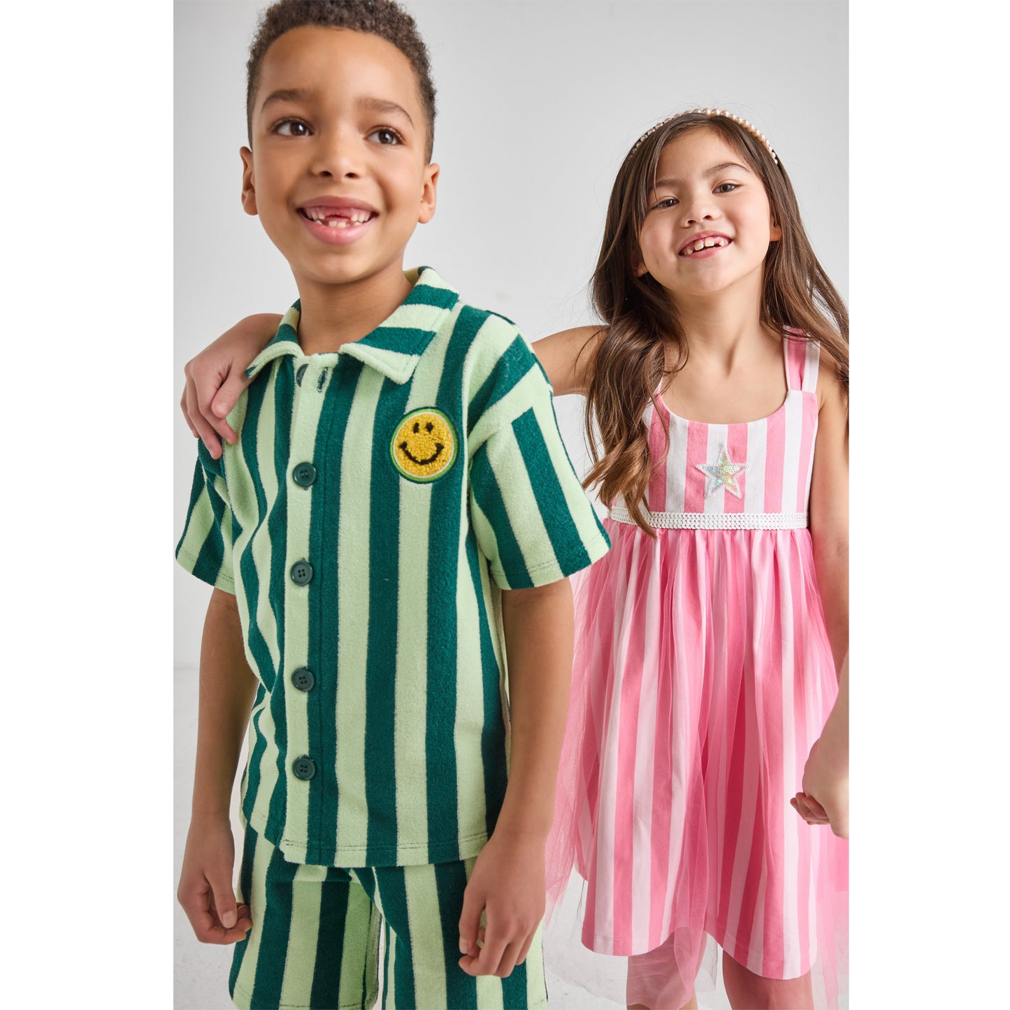A boy and a girl wearing sustainable green, pink, and white striped outfits.