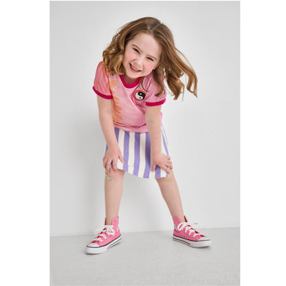 Girl in a sustainable pink tie-dye t-shirt and striped skort standing on a light gray background