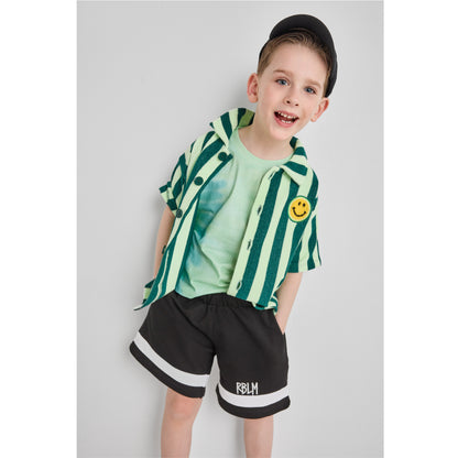 Boy wearing an organic cotton and recycled polyester green striped shirt with a smiley face and black shorts 