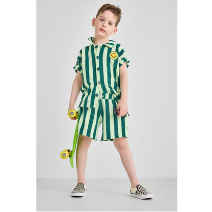 Boy wearing a sustainable, bright green striped set with a smiley face design, holding a skateboard