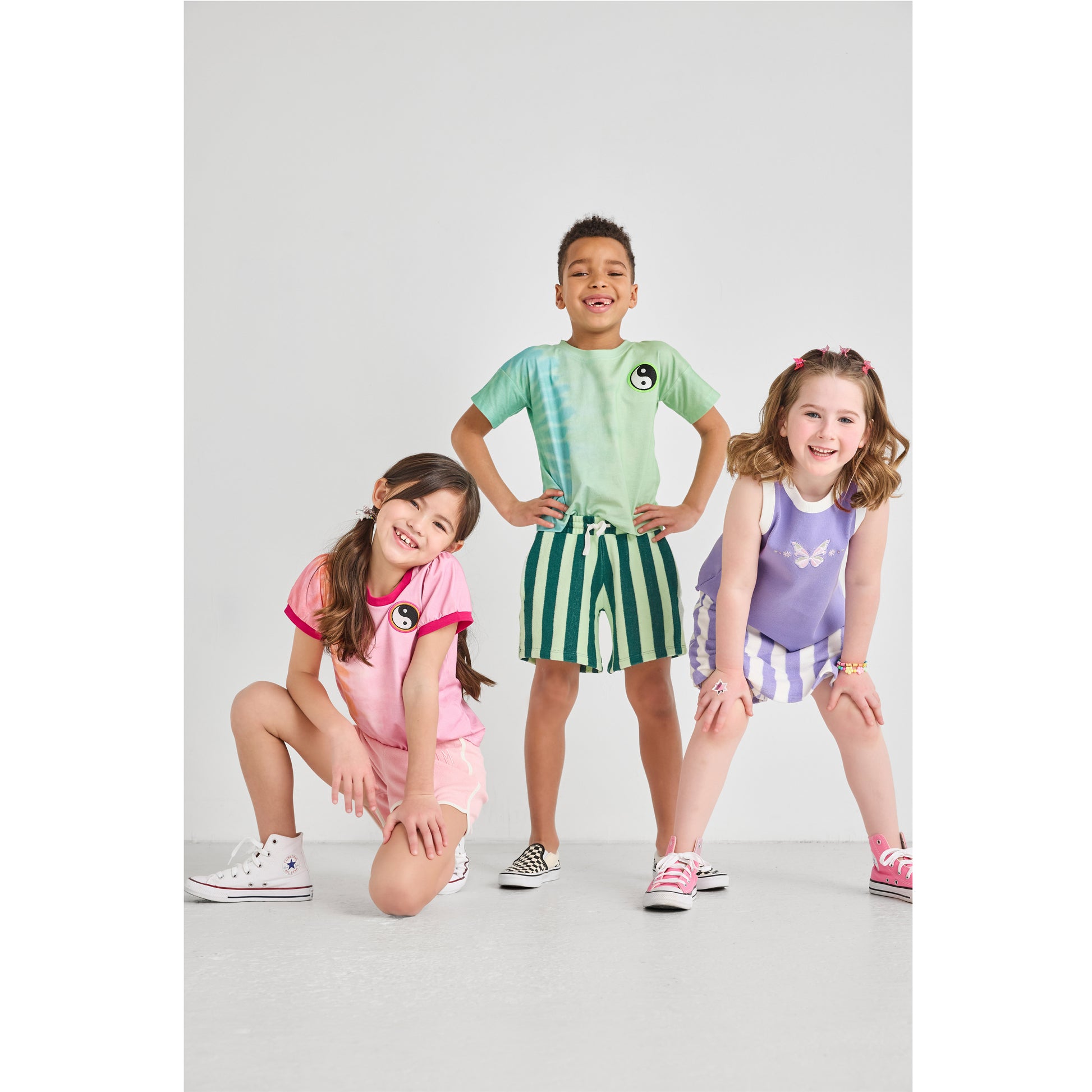 Three children, smiling, wearing colorful and sustainable outfits