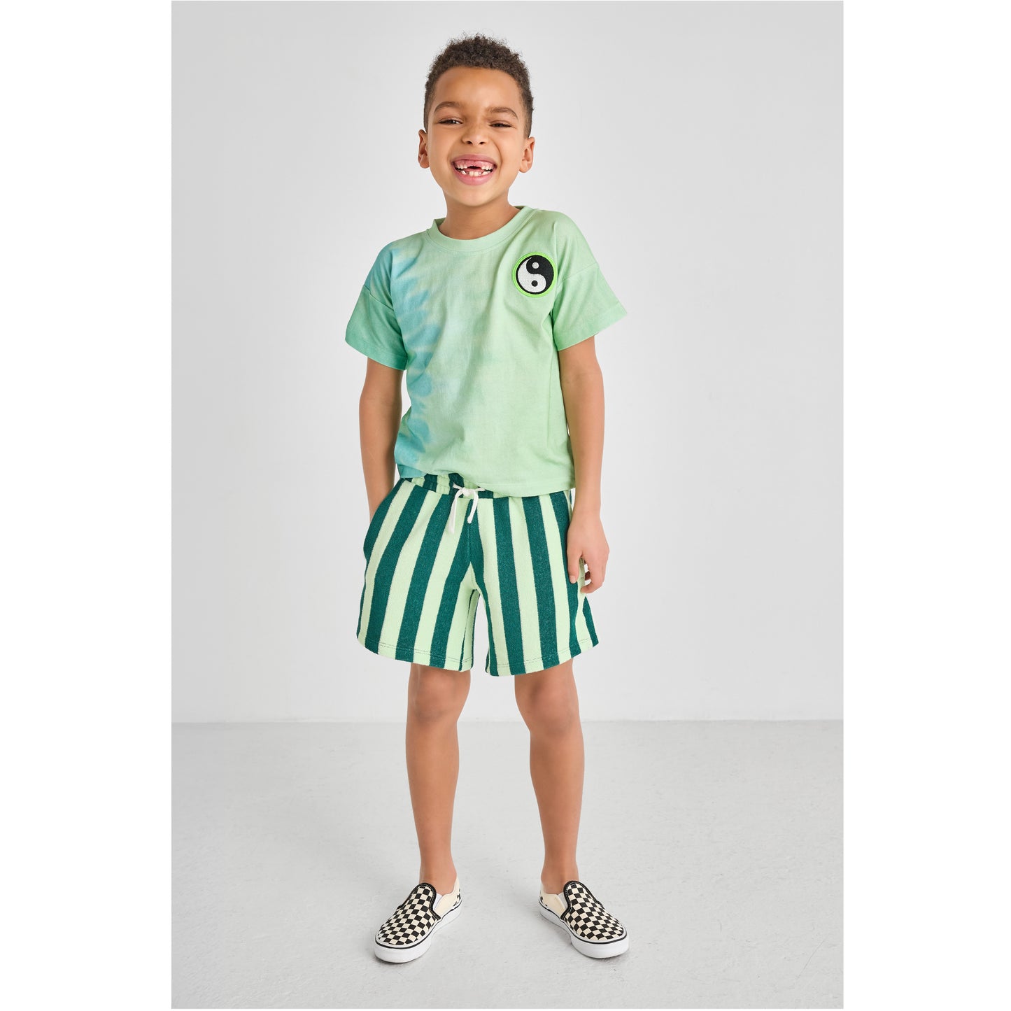 Child wearing a sustainable, colorful, green tie-dye shirt and striped shorts 